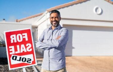 Hispanic real estate agent standing near sold sign outside house